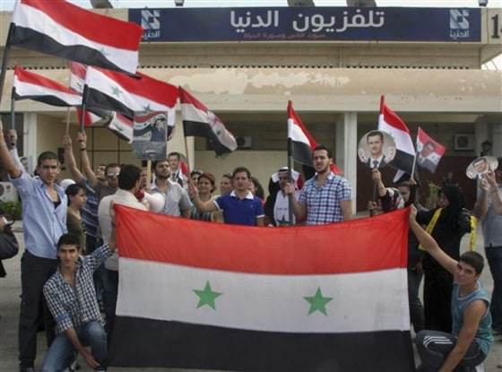 Pro-Syrian regime protesters hold Syrian flags and portraits of Syrian President Bashar Assad, as they protest to show their support for the Addounia pro-regime TV channel, on the airport highway near Damascus, Syria.